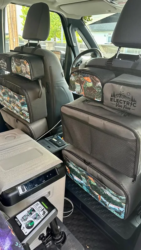 Inside the van: patterned seat-back organizer bags with the Electric Van Fam logo on both front seats, a fridge between them.