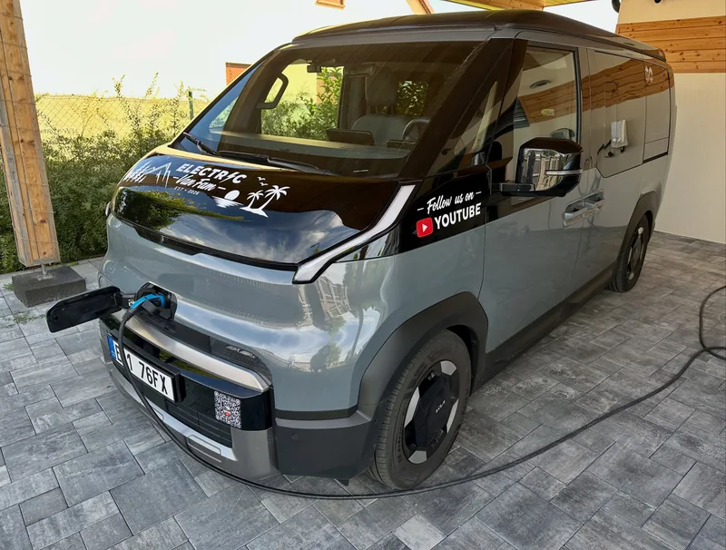 The grey van with its new black bonnet wrap, Electric Van Fam logo and “Follow us on YouTube” decal, charging on a driveway.